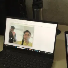 A student's face is framed by a green box on a laptop screen, demonstrating a face detection program they built using Python and AI libraries.