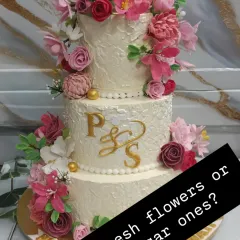 This three-tiered wedding cake features a textured buttercream finish and a cascade of handmade sugar flowers in shades of pink and burgundy. I prefer using sugar flowers for safety and artistry, ensuring every detail is beautiful and food-safe.