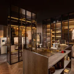 This island wardrobe is stripped down to its essential elements: aluminium profiles, brown-tinted glass, and succupira veneer. The shelves inside are glass and feature concealed lighting to beautifully showcase the contents.