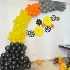 A creative construction-themed balloon arch using black, yellow, and orange balloons to simulate smoke, with gear cutouts on the wall.