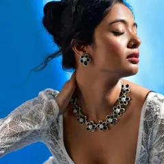 This image showcases a full jewelry set, including the necklace and matching earrings. The model's serene expression and the soft lighting on her skin create an elegant mood, while the bold blue background makes the black and white floral jewelry pop.