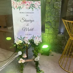 An elegant welcome sign for a Roka ceremony. The sign is placed on a wooden easel and decorated with a beautiful garland of artificial flowers and leaves.