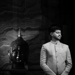 A moody and artistic black and white portrait of the groom. The dramatic lighting and the presence of the Buddha statue add a sense of calm and contemplation.