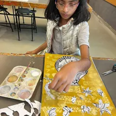 This student is arranging her black and white cut-outs onto a painted yellow background, creating a dynamic still life collage.