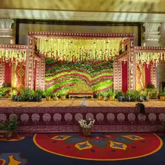 A beautiful example of a traditional stage for a wedding ceremony. The design features a rich floral backdrop using red and green flowers, framed by structures draped in classic wedding colors and patterns.