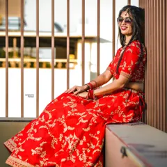 A modern bride takes a moment. Dressed in a stunning red lehenga and sunglasses, she relaxes against a modern slatted wall, bathed in golden hour light.