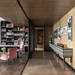 The corridor in the Caitriona apartment, where the flooring transitions from marble to a herringbone wood pattern. A striking 'Missoni Console' with mother-of-pearl inlay stands against a wall of family photos, blending personal touches with high design.