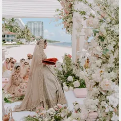 A beautiful wide shot of a beachside Anand Karaj ceremony. The bride is surrounded by flowers and family, with the ocean as a stunning backdrop.