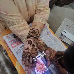 A Karwa Chauth design in progress. You can see the classic motif of a woman with a sieve, being drawn carefully on the palm, with a phone used for design reference.