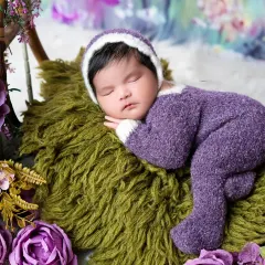 Dreaming in a field of lavender. This newborn is dressed in a cozy purple outfit, surrounded by beautiful floral arrangements for a vibrant and gentle portrait.