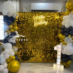 I designed this glamorous and modern birthday backdrop using a gold shimmer wall. The setup is framed by an organic balloon garland in black, white, and gold, and features a 'Happy Birthday' neon sign and a large marquee number '1' to mark the special occasion.
