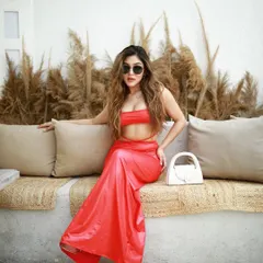 A seated pose from the red dress shoot, showcasing the full outfit against a rustic, bohemian-style bench.