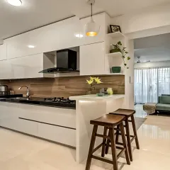 This open kitchen design includes a breakfast counter with stylish wooden stools, perfect for quick meals. The all-white, high-gloss cabinets make the space feel bright and spacious, connecting seamlessly with the living area.
