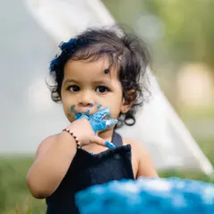 A sweet close-up of a baby girl with blue frosting on her hands and around her mouth. Her direct gaze into the camera makes this an engaging and adorable cake smash portrait.