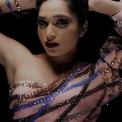 A close-up from a student designer collection, focusing on the shimmer and shine of the garment. The lighting is set to catch the sparkle of the sequins, highlighting the detailed craftsmanship of the one-shoulder top.