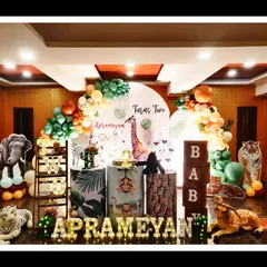 Aprameyan's second birthday was a jungle celebration filled with realistic animal figures and lush greenery. The setup includes marquee letters, themed pedestals, and a balloon arch in jungle-inspired colors, creating a fun and photogenic party space.