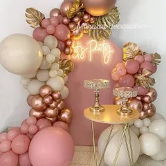 A chic arrangement featuring a pink backdrop with a 'Let's Party' neon sign. The organic balloon garland in shades of pink, cream, and rose gold is accented with gold palm leaves for a tropical glam look.