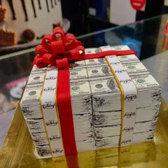 A cake that looks like a million bucks. This design is sculpted to resemble two large stacks of US hundred-dollar bills, wrapped with a red fondant ribbon.
