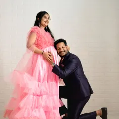 A classic pose for a maternity photoshoot, made even more special with our coordinated outfits. The expecting mother is wearing a beautiful pink ruffled gown, while her partner's suit complements her look perfectly.
