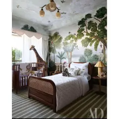 This image from the AD spread showcases the room's layout, with the woven cane bed and classic wooden crib set against the immersive, hand-painted jungle walls.