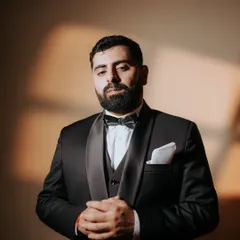A portrait of the groom, looking sharp and ready for the celebration. The dramatic lighting highlights his classic tuxedo, capturing a moment of quiet confidence on his engagement night.