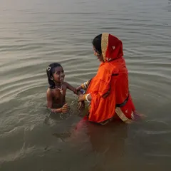 A mother and child share a moment of joy in the holy water during Chhath Puja, a candid photograph capturing the blend of ritual and family life.
