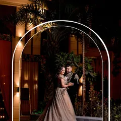 An elegant outdoor portrait at an evening engagement party. The archway frames the couple beautifully, and the lighting creates a sophisticated and opulent mood.