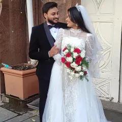 A beautiful moment from a Christian wedding. Our bride is wearing a delicate lace gown with long sleeves and a full tulle skirt, complemented by the groom's classic black tuxedo. I help couples find perfectly coordinated outfits for their special day.