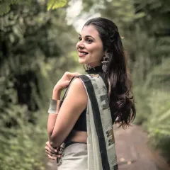 A moment of classic elegance. This outdoor portrait captures a modern woman in a traditional saree, using soft natural light to create a timeless and serene image against a lush green backdrop.