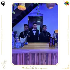 Three of our professional bartenders posing behind a rustic wooden bar. Their smart attire and confident stance reflect the high standards of service we provide for all types of events.