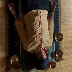 A client in a state of complete rest during a sound bath. An eye pillow helps to minimize external distractions, allowing the body to fully absorb the healing vibrations of the bowls placed around the head and torso.