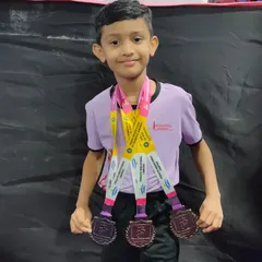 A young champion proudly displays the three medals he won at the Bhausaheb Navodit Gymnastics Competition. His success is a result of his dedication, discipline, and passion for the sport.