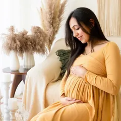 A close-up shot of an expecting mother cradling her bump, seated on a couch in a boho-styled corner of the studio. The textures of the pillows and blankets add to the cozy feel.