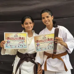 Two friends celebrate their promotion together, proudly displaying their new brown belts and certificates. The bonds formed in the dojo are as strong as our techniques.