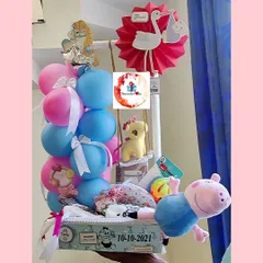 A cheerful "new arrival" hamper packed with essentials and toys for a newborn. This arrangement includes a Peppa Pig plush toy, baby clothes, and is decorated with pink and blue balloons and a stork cutout.