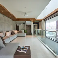 The family lounge in 'Wilasa' features a concrete-paneled accent wall and a large sectional sofa. The full-length glass balcony offers expansive views and fills the room with natural light.