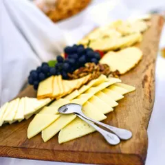 A rustic wooden board laden with a variety of cheeses, grapes, and walnuts. This makes for a perfect savory dessert course or a sophisticated addition to a wine and cheese event.
