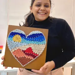 The joyful result of a creative date night. This participant is all smiles with her completed heart-shaped landscape string art.