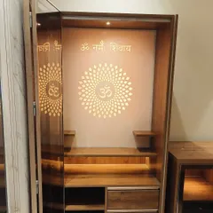 A close-up of the mandir with its doors open, revealing the intricately cut, backlit panel with 'Om Namah Shivay'. The design includes shelves for idols and drawers for storing pooja samagri.