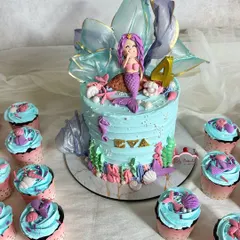 Here's a closer view of the pastel mermaid cake, highlighting the shimmering, translucent sugar sail and the adorable fondant mermaid. The sides of the cake are decorated with colorful coral and seashells.