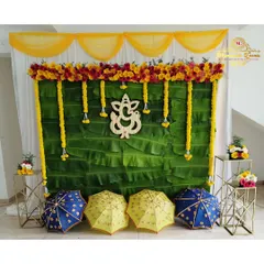 A classic backdrop for a naming ceremony or puja, using a wall of banana leaves, marigold garlands, and a wooden Ganesha cutout.