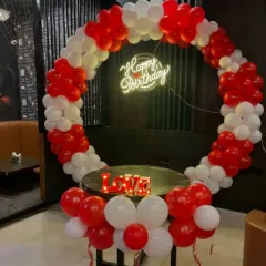 A romantic red and white balloon ring setup. This decoration is perfect for an anniversary or a birthday, featuring a 'Happy Birthday' neon sign and a 'LOVE' marquee sign.