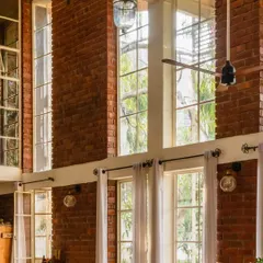 The double-height windows at The Brick Loft flood the space with natural light. The exposed brickwork and sleek window frames create a beautiful contrast, while the greenery adds to the cozy, inviting atmosphere.