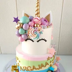 A magical unicorn cake designed for a fifth birthday celebration. This two-tiered creation features a pastel rainbow striped bottom tier, a sleepy unicorn face on the top tier, and is decorated with a golden horn, floral details, and candy-colored spheres.