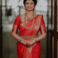 A stunning portrait of the bride on her engagement day, dressed in a vibrant red silk saree and traditional gold jewelry.