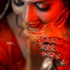 A detailed close-up of the bride's face, focusing on her intricate henna and nath. The dramatic red lighting adds a touch of romance and intensity.