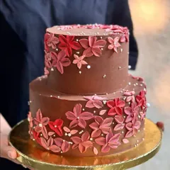 This two-tiered chocolate wedding cake features a cascade of hand-piped flowers in shades of red and pink. The rich chocolate buttercream provides a beautiful contrast, making it a bold and romantic choice for a celebration.