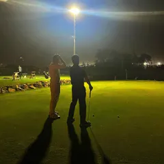 Two players discuss strategy on the putting green under the bright floodlights. The game doesn't stop when it gets dark here.