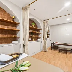 This view showcases the flow between different treatment zones in the Vedic Spa. You can see the traditional Shirodhara station in the background, seamlessly integrated with modern massage beds and storage, ensuring both functionality and a serene aesthetic.