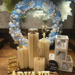 A cool-toned birthday decoration featuring a balloon ring of pastel blue, white, and silver, complemented by a 'Happy Birthday' neon sign and 'B-A-B-Y' blocks.